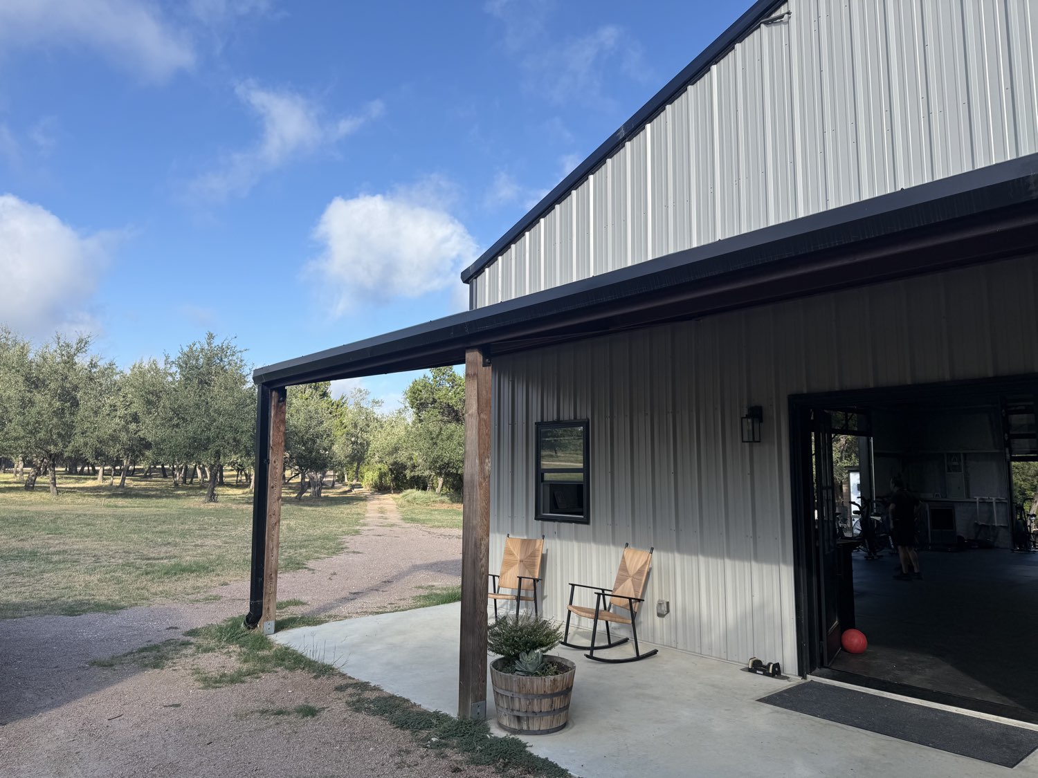 Custom metal ranch building with a covered porch on cedar posts, open pasture and oaks beyond